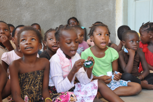 Eine Gruppe trauriger Kinder sitzt vor einem Gebäude mit einer Wand und einer Tür im Hintergrund.