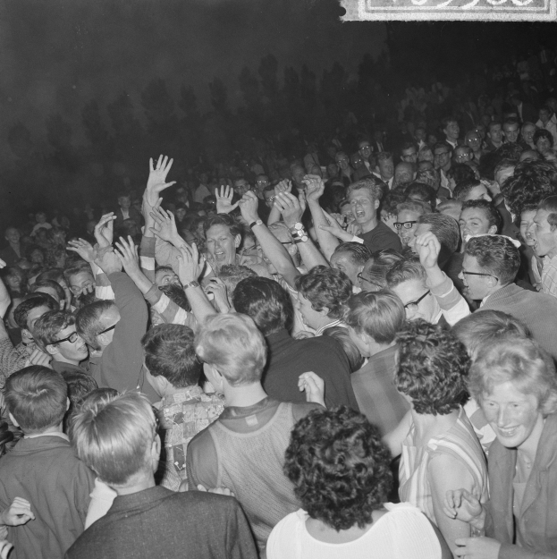 Ein Schwarz-Weiß-Bild einer Menge bei einem Konzert mit erhobenen Händen um eine Tafel mit Text.