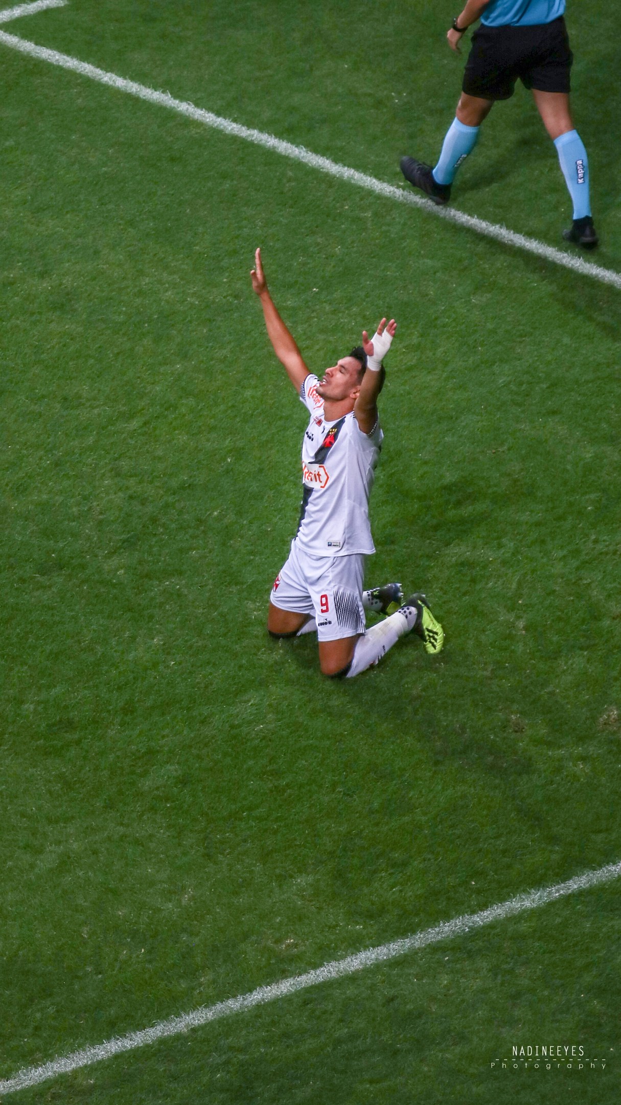 Ein Fußballspieler kniet auf dem Boden und streckt die Arme aus, um zu feiern, trägt eine Sportuniform und Fußballschuhe.