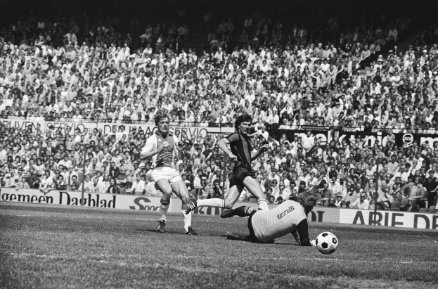 Schwarzes und weißes Foto von Fußballspielern auf einem Feld während eines Bundesliga-Spiels 1978-79 zwischen Ajax und Hannover 96, mit Zuschauern im Hintergrund.