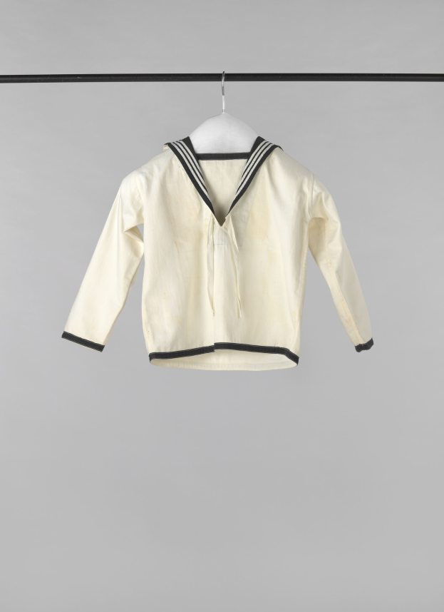 Weißer Matrosenstil-Jacke mit Kragen, langen Ärmeln und Knopfleiste, an einer Wäscheleine gegen einen weißen Hintergrund hängend.