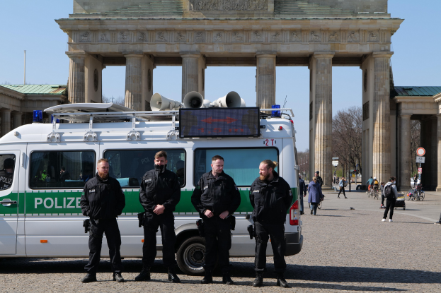 Polizisten in schwarzer Uniform vor dem Brandenburger Tor in Berlin, mit einem weißen und grünen Fahrzeug im Vordergrund und Fußgängern und Radfahrern im Hintergrund.