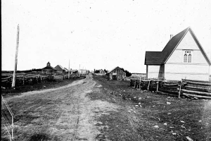 Ein Schwarz-Weiß-Foto einer Schotterstraße mit Häusern auf beiden Seiten, hölzernen Zäunen und Masten im Hintergrund, mit dem Text "St. Joseph's Church, St. Louis, Missouri" unten.