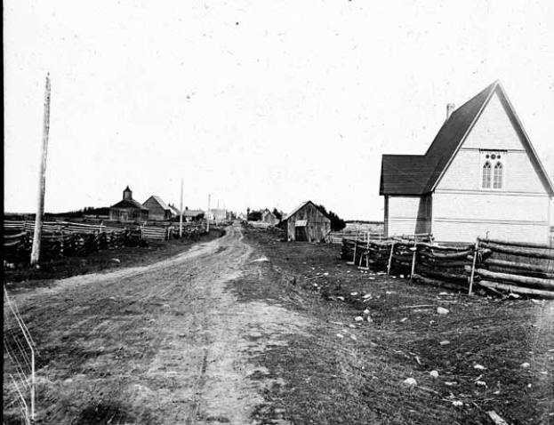 Ein Schwarz-Weiß-Foto einer Schotterstraße mit Häusern auf beiden Seiten, hölzernen Zäunen und Masten im Hintergrund, mit dem Text "St. Joseph's Church, St. Louis, Missouri" unten.