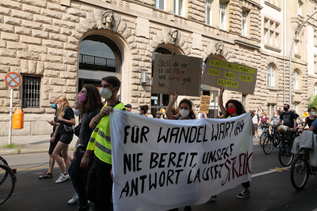 Eine Gruppe von Menschen marschiert auf einer Straße, einige halten Schilder und Banner, andere fahren Fahrräder, während sie an einer Protestaktion gegen die Anti-Kriegs-Bewegung in Berlin teilnehmen.