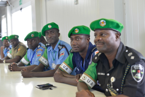 Eine Gruppe von Polizeibeamten sitzt an einem Tisch in einem Raum mit einer Wand, Fenstern links und einer Decke mit Lampen, mit Mobiltelefonen und anderen Gegenständen auf dem Tisch, was auf eine Schulung hinweist.