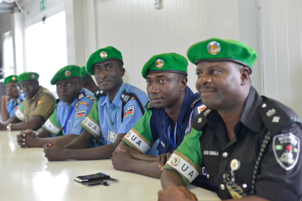 Eine Gruppe von Polizeibeamten sitzt an einem Tisch in einem Raum mit einer Wand, Fenstern links und einer Decke mit Lampen, mit Mobiltelefonen und anderen Gegenständen auf dem Tisch, was auf eine Schulung hinweist.