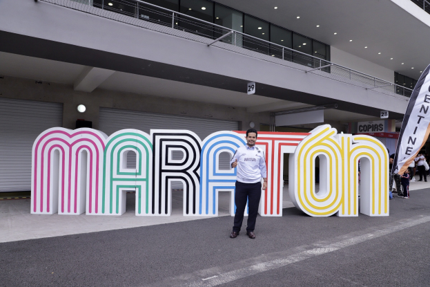 Ein Mann, der vor einem "Marathon"-Schild lächelt, umgeben von Menschen mit Schildern und einem beleuchteten Gebäude im Hintergrund.
