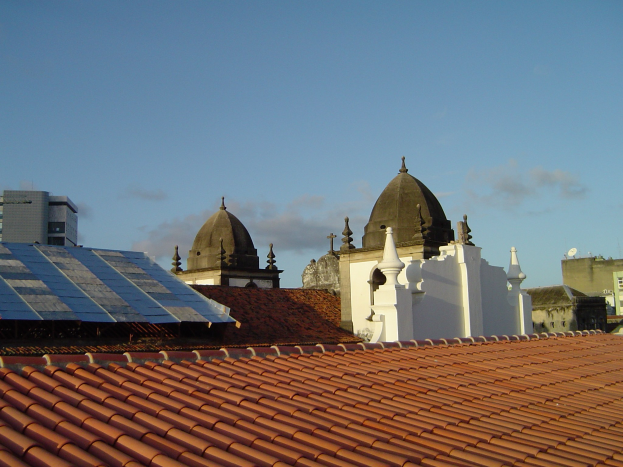Stadtansicht mit mehreren Gebäuden im Vordergrund, einem klaren blauen Himmel im Hintergrund und Solarpaneelen auf einem Dach.