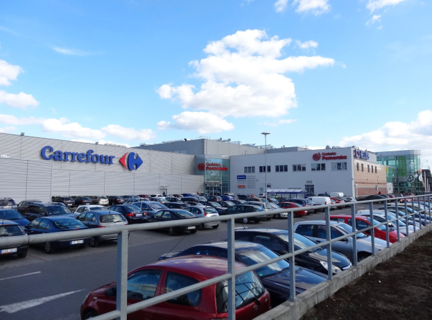 Großes Autohaus mit mehreren parkenden Fahrzeugen vorne, umgeben von städtischen Gebäuden, Straßeninfrastruktur und Fahrzeugen auf der Straße.