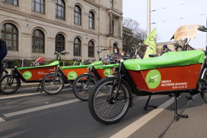 Eine Gruppe von Fahrrädern, die an einer Straße geparkt sind, mit einer Person in der Nähe, vor einem Hintergrund aus Gebäuden, Bäumen und einem klaren Himmel, mit einem Fahrrad-Sharing-Banner im Vordergrund.