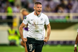 Ein Mann in einem weißen Hemd und schwarzen Shorts rennt auf einem Fußballfeld, umgeben von einer Gruppe von Menschen, die ein Tor in einem Spiel zwischen Leeds United und Melbourne Victory feiern.