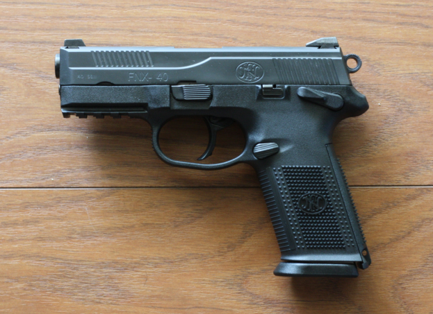 Eine schwarze Sig Sauer P320 X-Five 9mm halbautomatische Pistole mit einem strukturierten Griff und einem langen Lauf liegt auf einem hellen Holztisch.