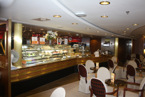 Ein Restaurant-Innenraum mit Tischen und Stühlen, einer Theke mit Blumenvasen, Tafeln mit Text, einem Ventilator und anderen Gegenständen unter einer Decke mit warmer Beleuchtung.