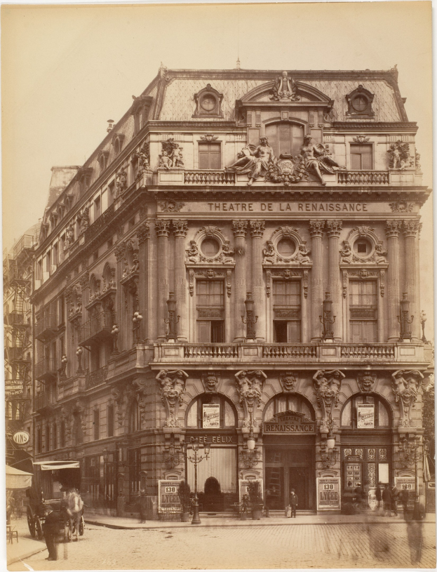Schwarz-weißes Foto des Théâtre de la Renaissance in Paris, das seine Fassade mit Fenstern, Säulen, Bögen und Skulpturen zeigt, mit einigen Menschen und Fahrzeugen auf der Straße davor und dem Himmel im Hintergrund.