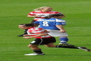 Drei Frauen in Sportuniformen beim Fussballspielen auf einem grünen Feld.