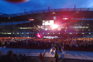 Konzerthalle mit Publikum, Scheinwerfern und Projektionsschirm.