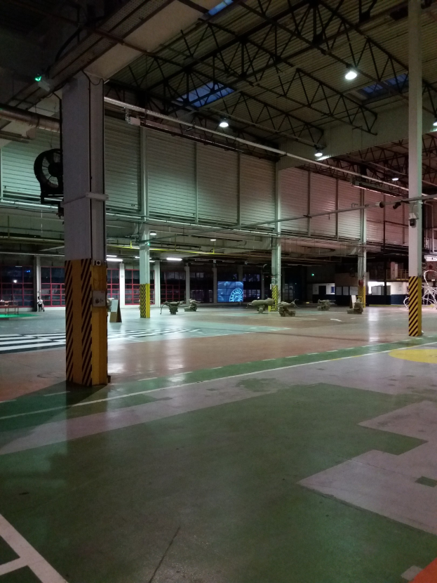 Großer Lagerraum mit verschiedenen Maschinen, Metallstangen und Beleuchtungsausrüstung, mit Text auf der rechten Bodenfläche.