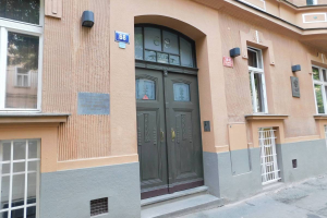 Ein Geb├Ąude mit einer gr├╝nen T├╝r und Fenstern an der Seite, das sich auf einer Stra├če mit einem Gehweg befindet, der zu ihm hinf├╝hrt, und Schilder und Lichter zeigt, die darauf hinweisen, dass es eine Wohnung zum Verkauf in der Innenstadt ist.