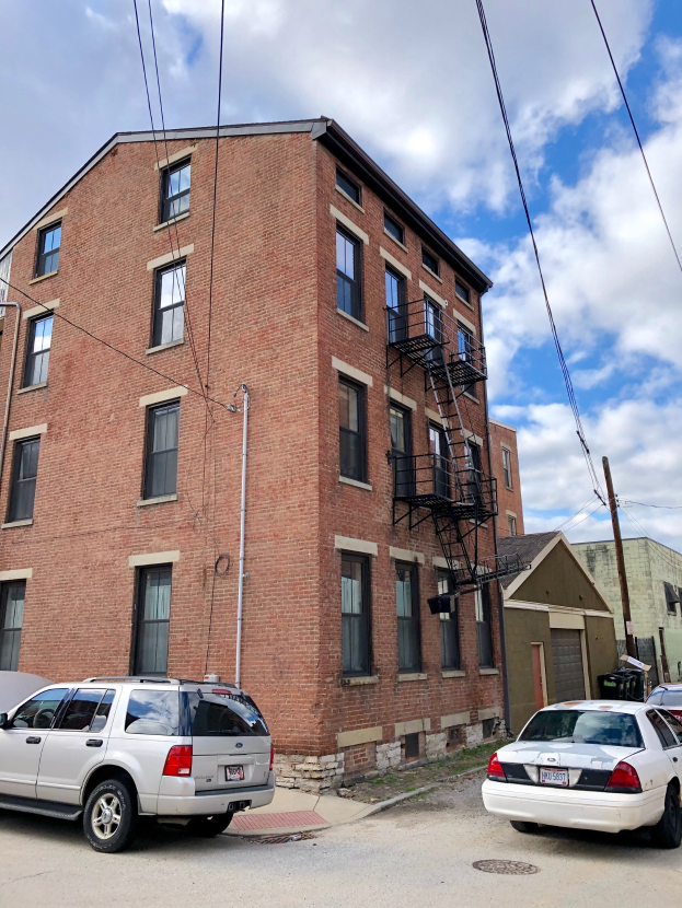 Ziegelgebäude mit Fenstern, Treppe mit Geländer und parkenden Autos davor, mit einem Mast mit Drähten im Vordergrund, einem bewölkten Himmel im Hintergrund und Text unten, der Wohnungen zur Miete an der Adresse 5901 S Elmwood Ave, Chicago 60618 auflistet.