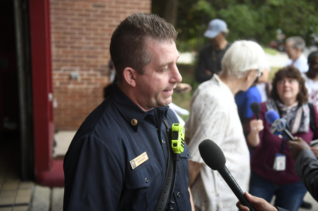 Polizeibeamter spricht mit Reportern vor Bäumen und einem Gebäude.