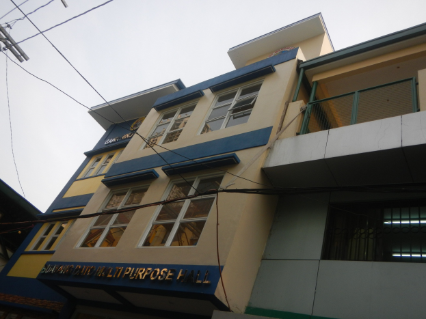 Mehrzweckgebäude mit blauer und gelber Fassade, Glasfenstern, einem Schild, einem Strommast mit Kabeln und einem klaren blauen Himmel im Hintergrund.
