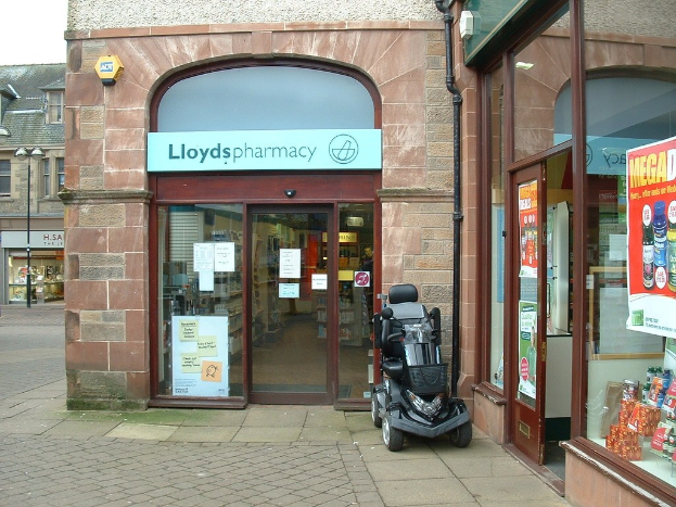 Apothekenladen mit einem vor dem Gebäude geparkten Auto und einem Gebäude auf der linken Seite.