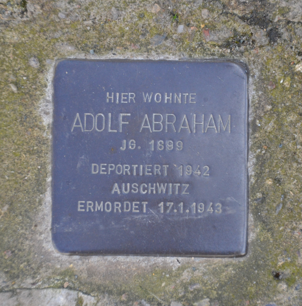Rechteckige Plakette mit der Inschrift "Adolf Abraham" an einer Steinwand angebracht.