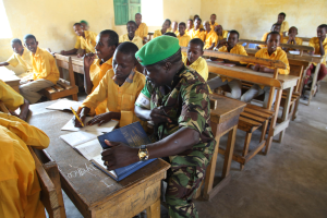 Eine Gruppe von Kindern sitzt an Tischen in einem Klassenzimmer mit Büchern und Stiften, ein Fenster im Hintergrund.