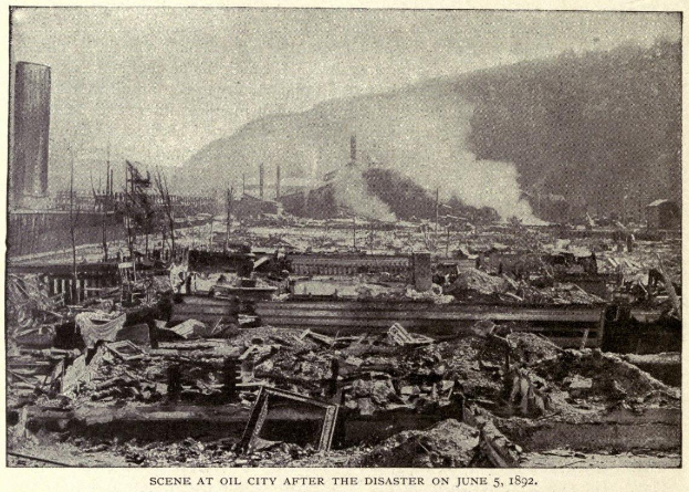 Schwarz-weiß-Foto einer Stadt nach einer Katastrophe am 5. Juni 1892, das beschädigte Gebäude, Strommasten, Rauch und einen Hügel im Hintergrund zeigt, mit Text unten.