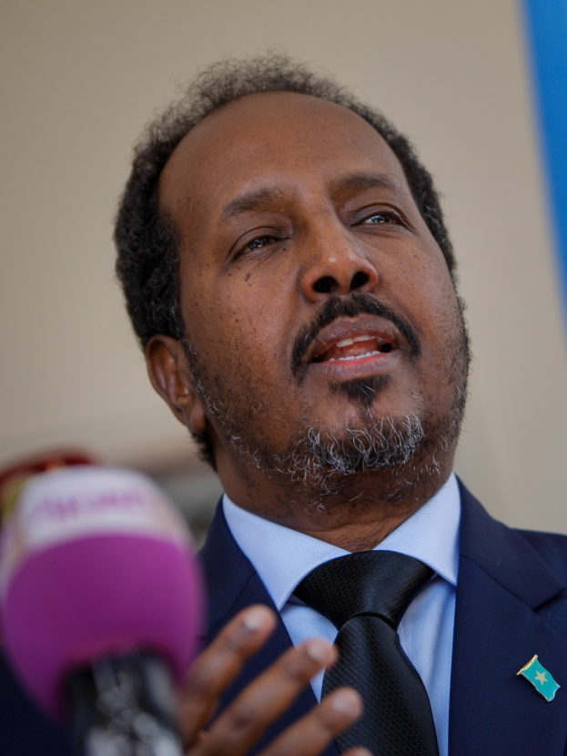 Ein Mann im Anzug und Krawatte, der in ein Mikrofon spricht und wahrscheinlich eine Zuschauermenge anspricht.