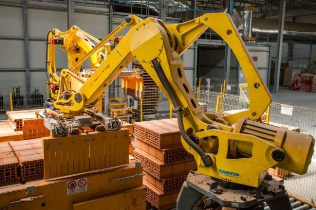 Großes Industrie-Lager mit gestapelten Kisten, Kränen an der Decke, Zaun, Pfosten und einer fernen Wand in einer Fertigungsumgebung.