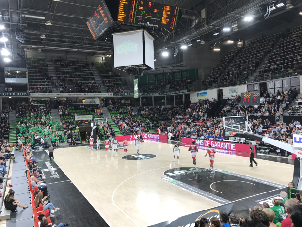 Basketballspiel zwischen Asvel und Galatasaray in einem vollen Stadion mit Anzeigetafeln, die die Teamnamen anzeigen.