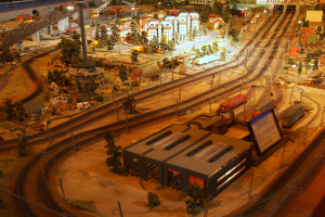 Eine Modellbahnanlage in einem Museum mit Gebäuden, Bäumen, Schienen, Fahrzeugen, Masten, Lampen, Plakaten und anderen Gegenständen, die eine belebte Stadtlandschaft schaffen.