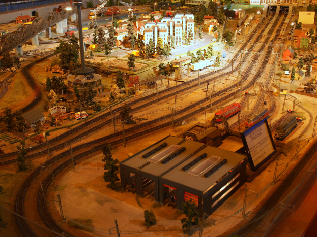 Eine Modellbahnanlage in einem Museum mit Gebäuden, Bäumen, Schienen, Fahrzeugen, Masten, Lampen, Plakaten und anderen Gegenständen, die eine belebte Stadtlandschaft schaffen.