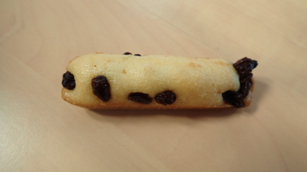 Ein Nahaufnahme eines goldbraunen Keks mit einer leichten Puderzuckerbestäubung und Rosinen auf einem Holztisch.