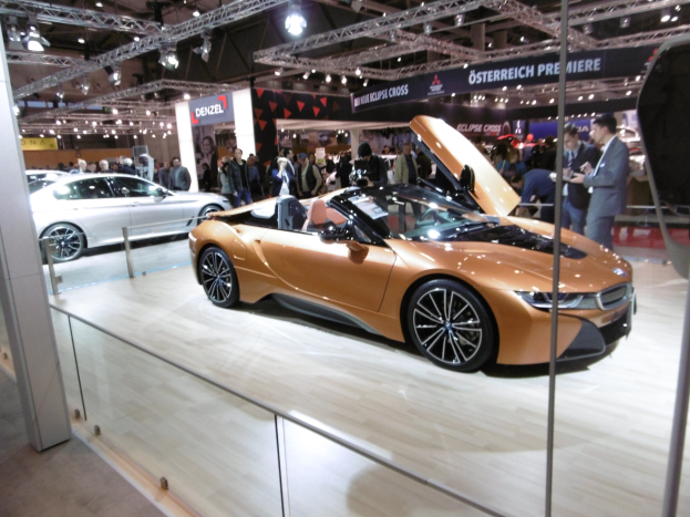 Schwarzer BMW i8 Roadster mit gl├Ąnzendem Finish und Chromakzenten auf der Frankfurt Motor Show umgeben von formell gekleideten G├Ąsten.