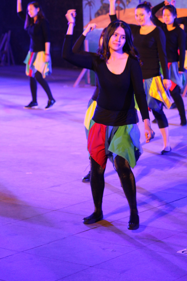 Eine Gruppe junger Frauen, die auf einer Bühne tanzen, mit einem Gemälde an der Wand im Hintergrund.