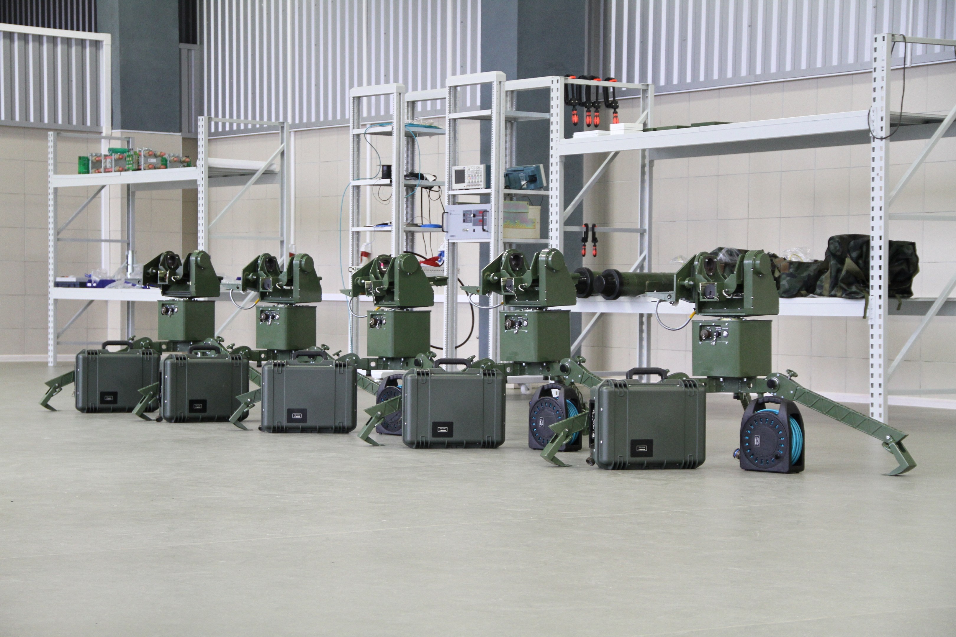 Gruppe von Milit├Ąrrobotern auf einem Boden mit Koffern und Gegenst├Ąnden auf Gestellen, positioniert gegen eine Wand mit einem Gel├Ąnder im Hintergrund.