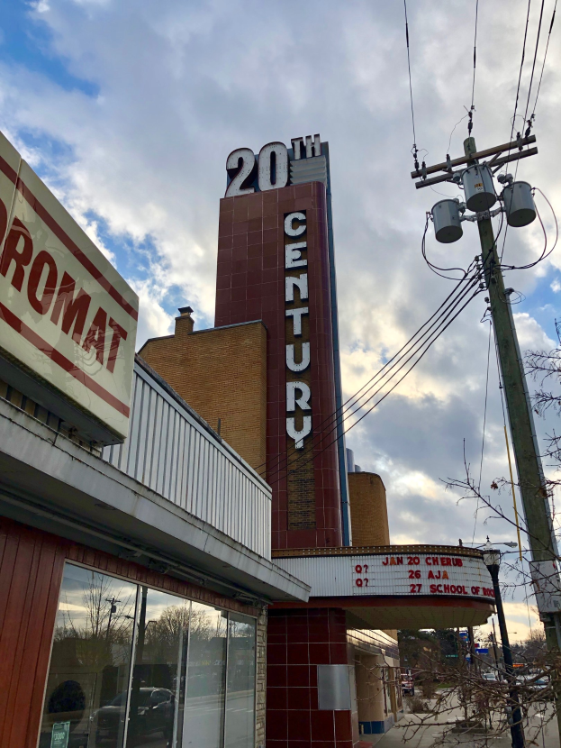 Außenansicht des 20. Jahrhundert Theaters in Detroit, Michigan, mit Glaswänden und Namensschildern, umgeben von Bäumen, Strommasten und Drähten sowie einem bewölkten Himmel im Hintergrund.