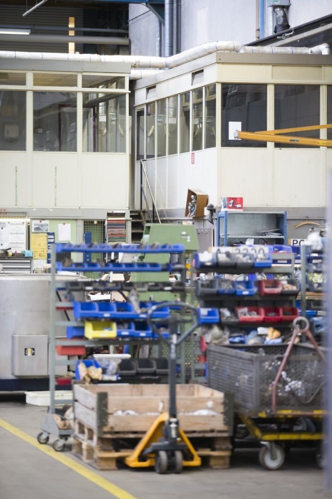 Großes Lagerinnere mit verschiedenen Geräten einschließlich fahrbaren Wagen, Schränken und einer Box, mit einer Glasfensterwand und freiliegenden Rohren im Hintergrund.
