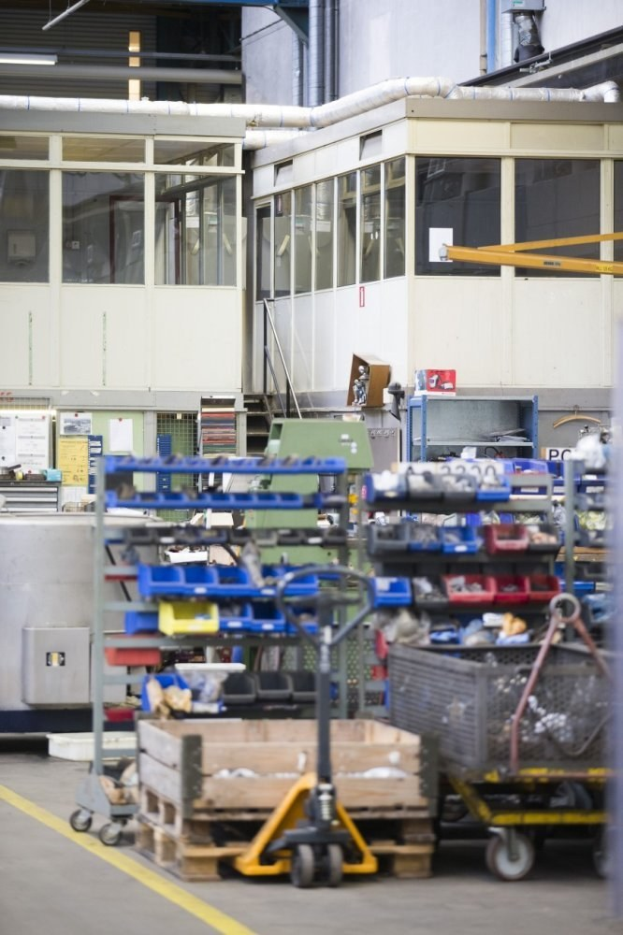 Großes Lagerinnere mit verschiedenen Geräten einschließlich fahrbaren Wagen, Schränken und einer Box, mit einer Glasfensterwand und freiliegenden Rohren im Hintergrund.