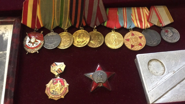 Ein hölzerner Kasten mit verschiedenen Medaillen, darunter ein roter Stern, ordentlich angeordnet mit einem Objekt auf der rechten Seite.