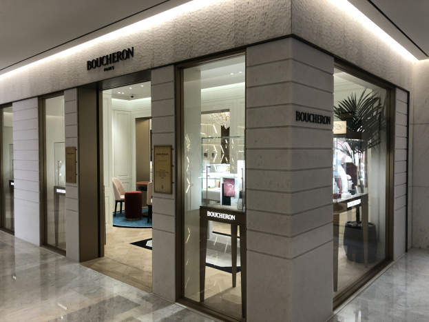 Eintritt in ein Boutique in einem Einkaufszentrum mit Glaswänden und -türen, beleuchteter Decke, Möbeln, einer Pflanze und sichtbarem Boden.