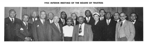 Eine Gruppe von Männern in Anzügen, die vor einer Wand stehen und lächeln, mit Text oben und unten '1955 Zwischenversammlung des Kuratoriums', in Schwarz-Weiß.