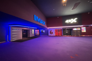 Innenseite eines Kinos mit lila Teppich, Wänden mit Text und Bildschirmen sowie Deckenbeleuchtung.