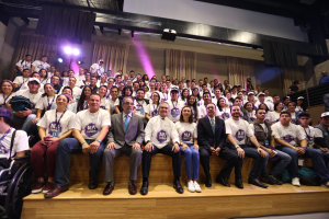 Eine Gruppe von Menschen sitzt auf einer Bühne mit einer Person im Rollstuhl links, mit Vorhängen, Scheinwerfern und einer Wand im Hintergrund bei der Nationalen Konferenz der Frauenbasketball-Vereinigung.
