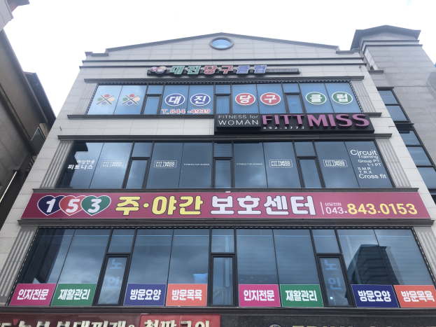 Ein Gebäude in Seoul, Südkorea, mit einem Schild, auf dem "Fitness für Frauen" steht, Fenstern und textbedeckten Tafeln im Hintergrund des Himmels.