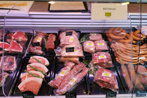 Eine Vitrine in einem Metzgerladen mit verschiedenen Fleisch- und Wurstwaren in Schalen, jede mit Preisschildern, und ein Textschild im Hintergrund.