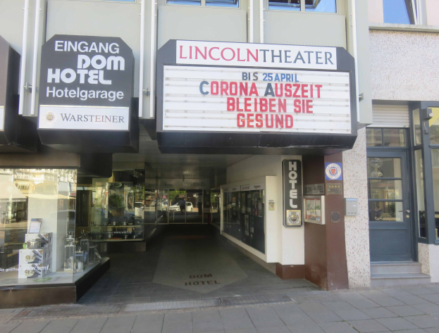 Außenansicht des Lincoln Theaters in Berlin, Deutschland, mit Glasfenstern und -türen sowie einer Tafel und einem Inneren, das eine pulsierende Stadtlandschaft vermuten lässt.